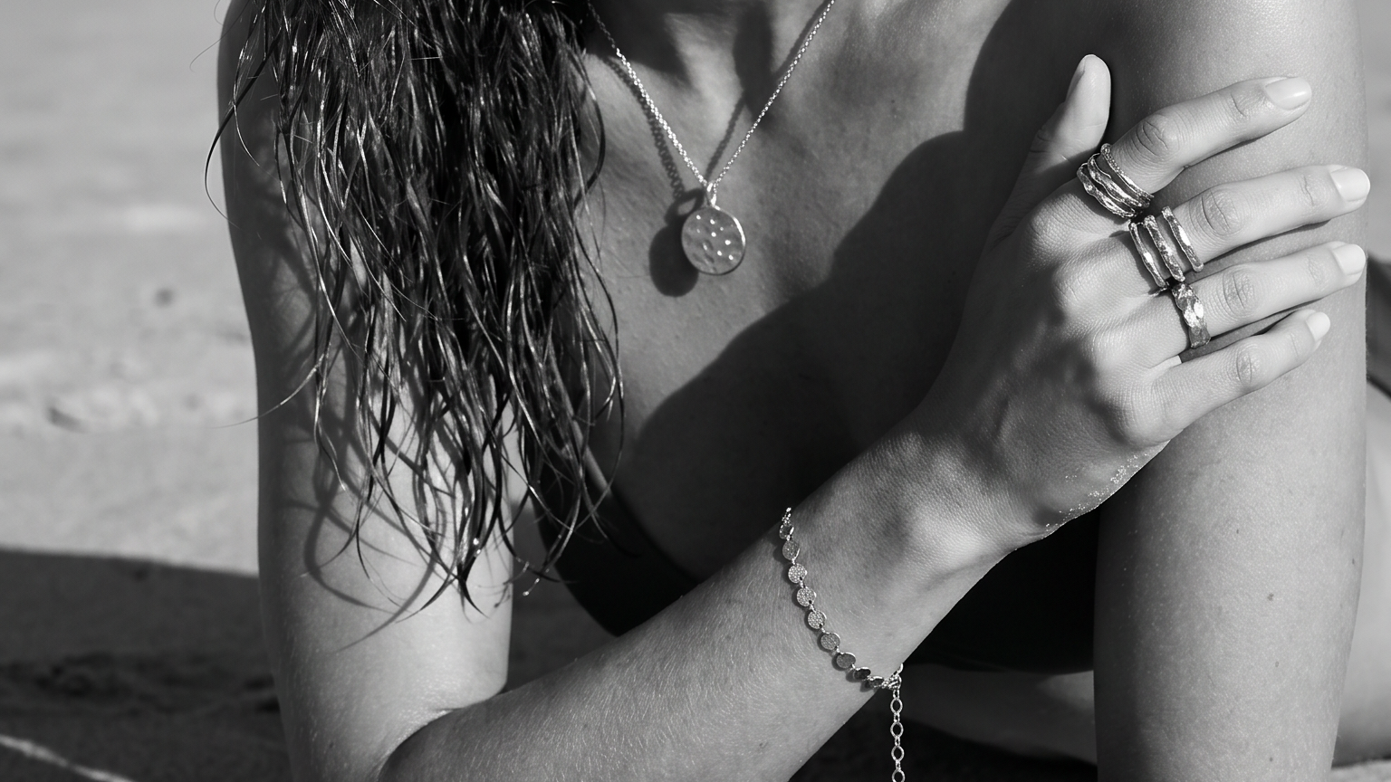 Gold jewellery worn near the ocean in natural sunlight.