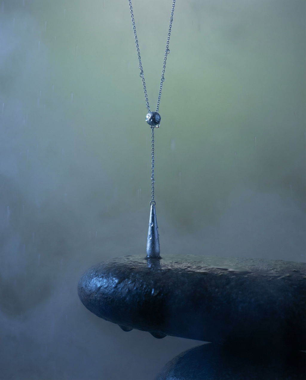 Silver lariat necklace sculptural jewellery pendant hanging from a chain on a blurred natural background