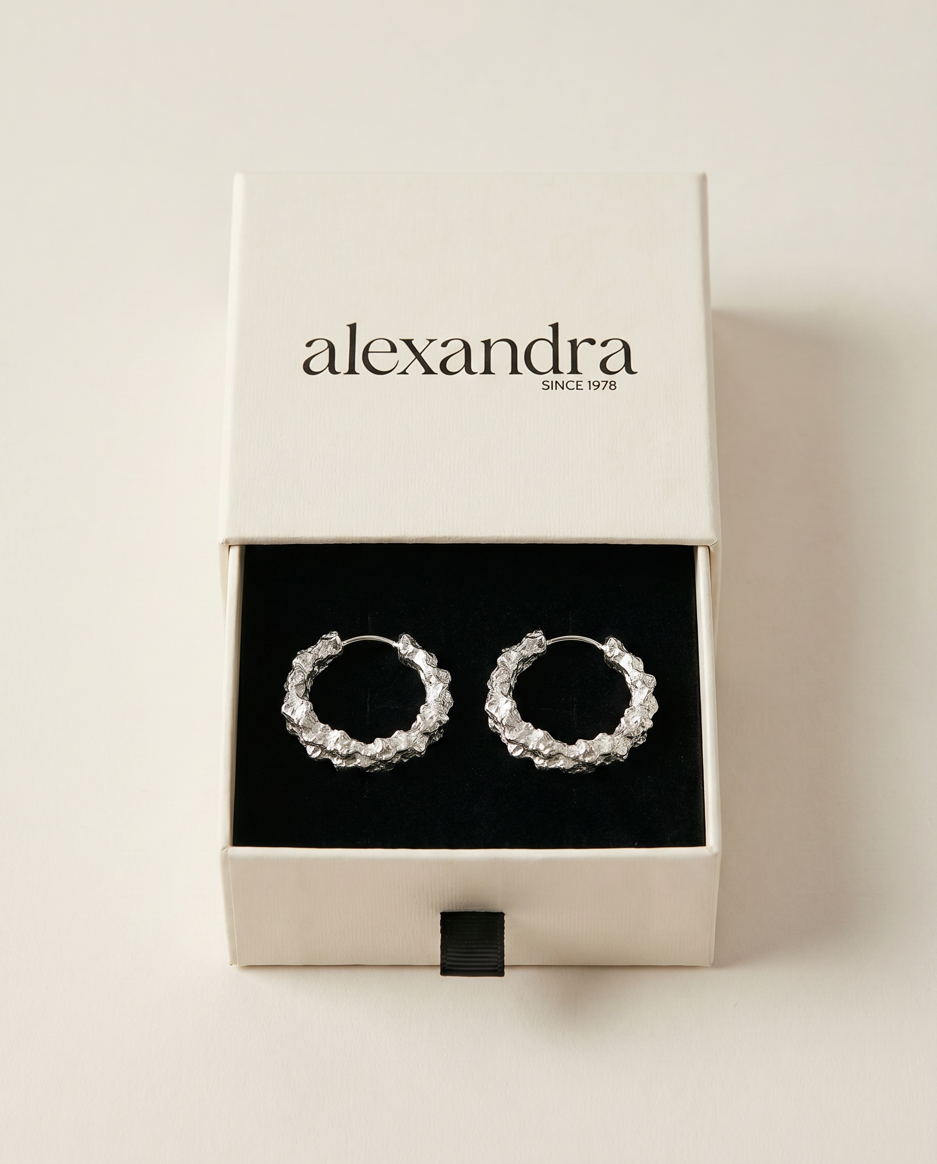 Pair of silver hoop earrings in a 'alexandra' branded box on a light beige background