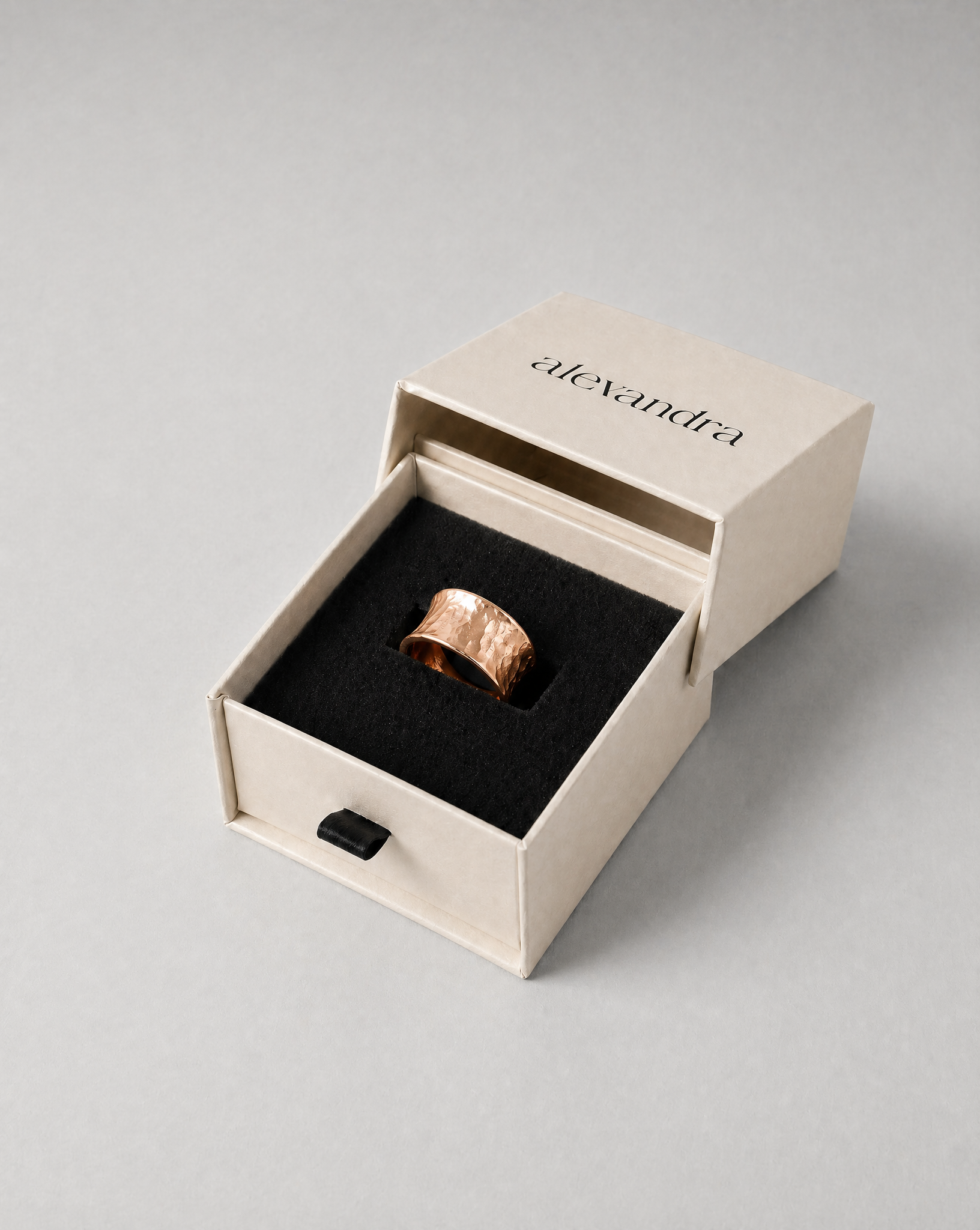 Raw Rose gold ring in a 'alexandra' branded box on a gray background