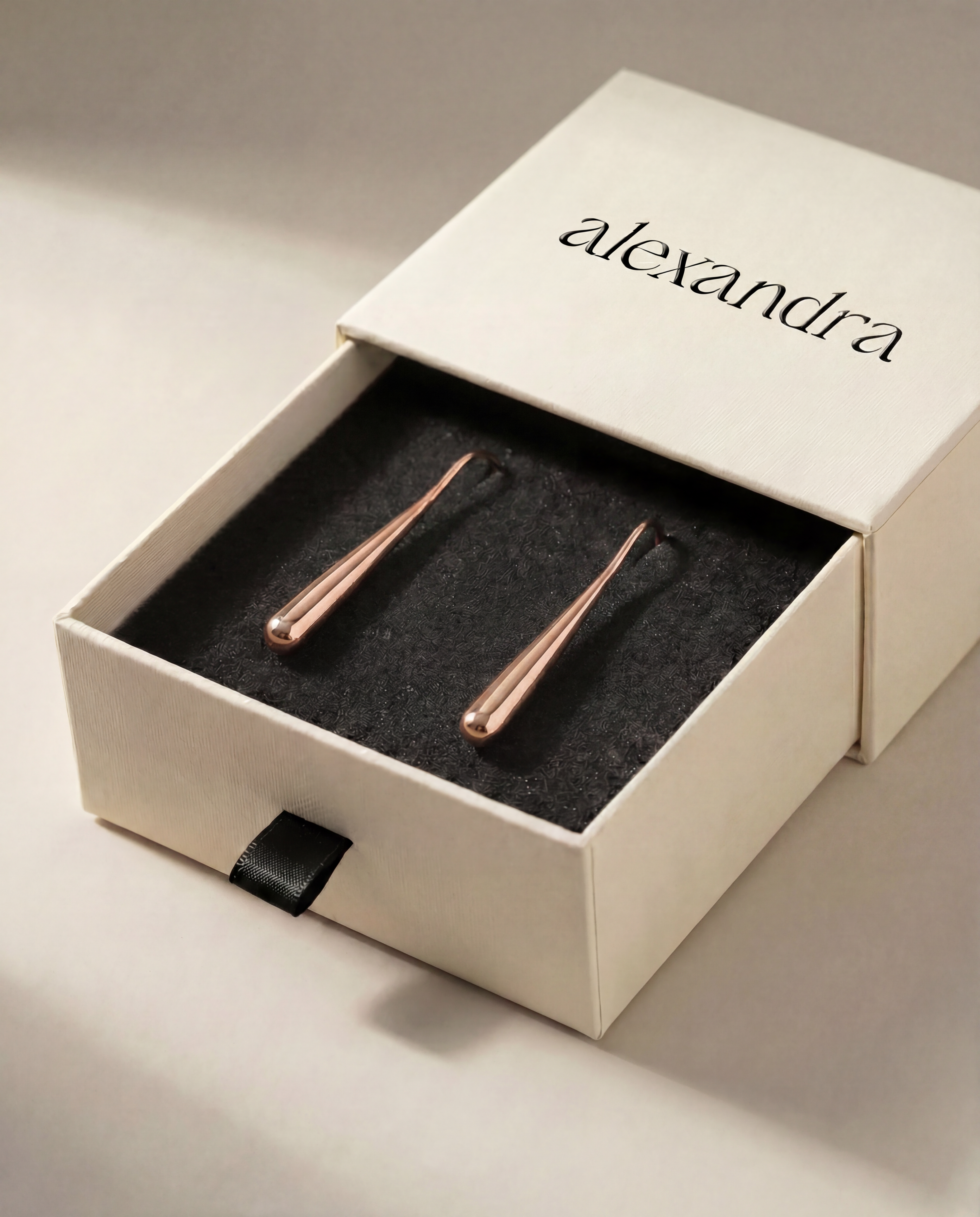 Rose gold earrings in a 'alexandra' branded box on a neutral background