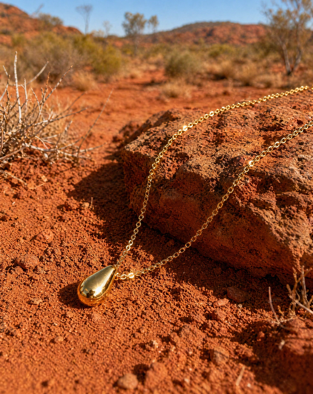 Refined Gold necklace with a teardrop pendant on red dirt with desert landscape in the background