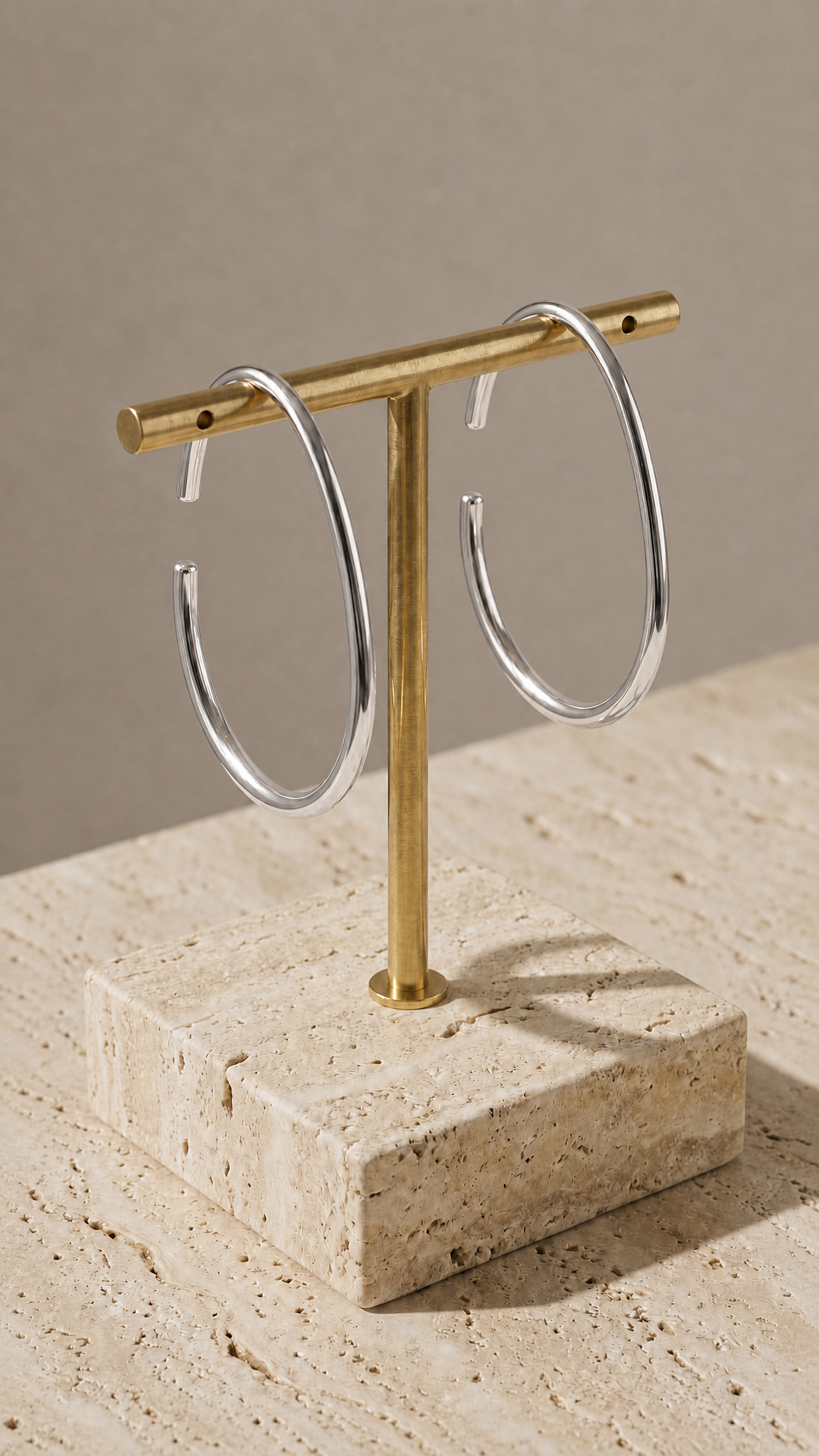 Gold T-shaped jewelry stand with delicate silver hoop earrings on a beige surface.