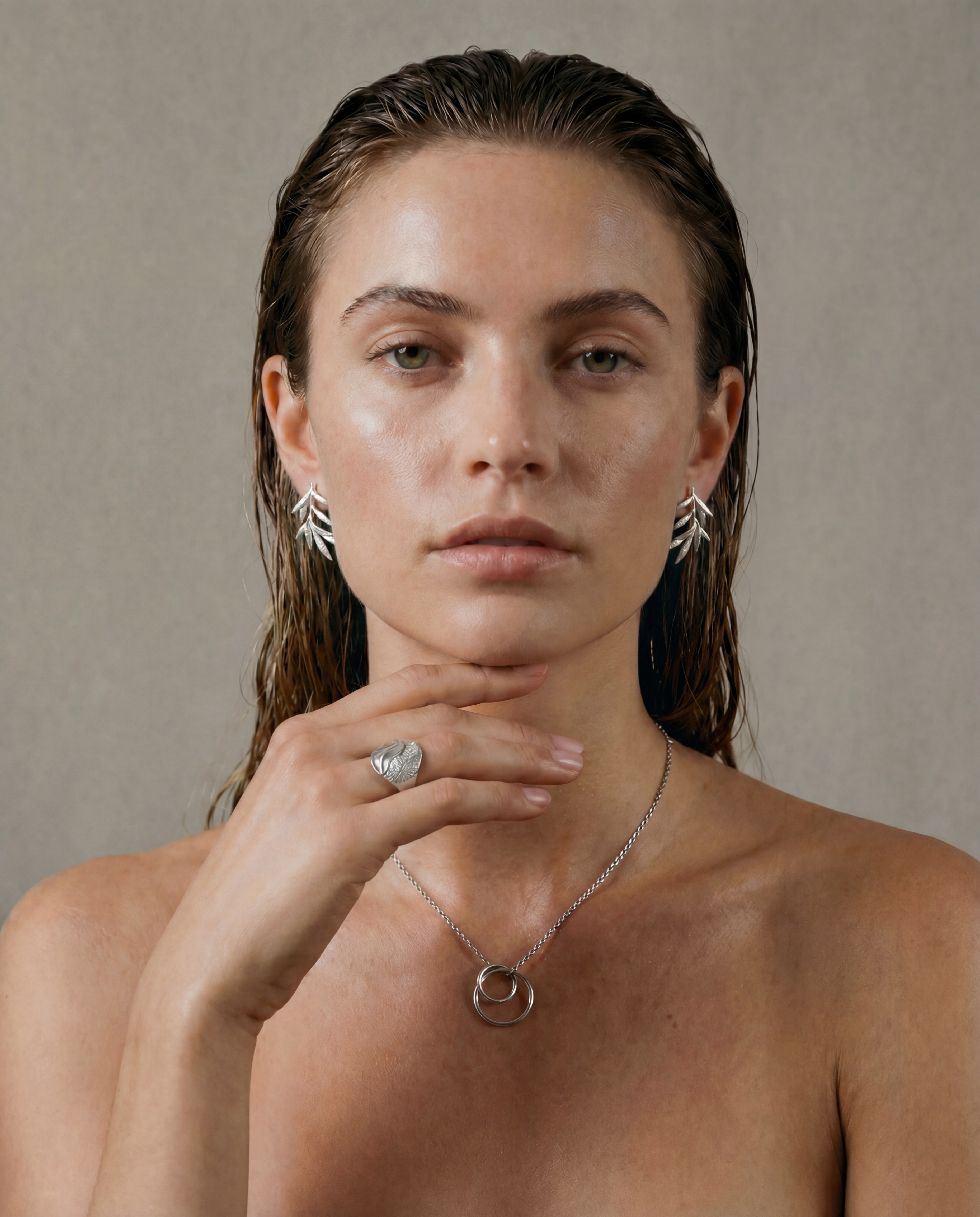 Woman wearing delicate silver earrings and a necklace against a neutral background