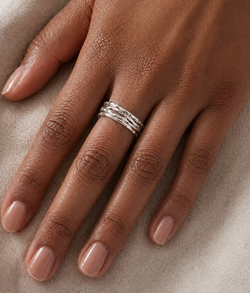 Hand wearing refined silver ring on a neutral background