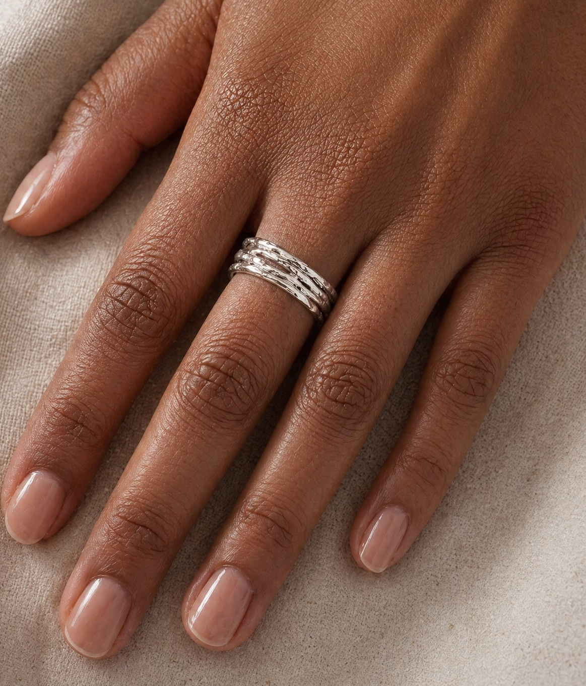 Hand wearing refined silver ring on a neutral background