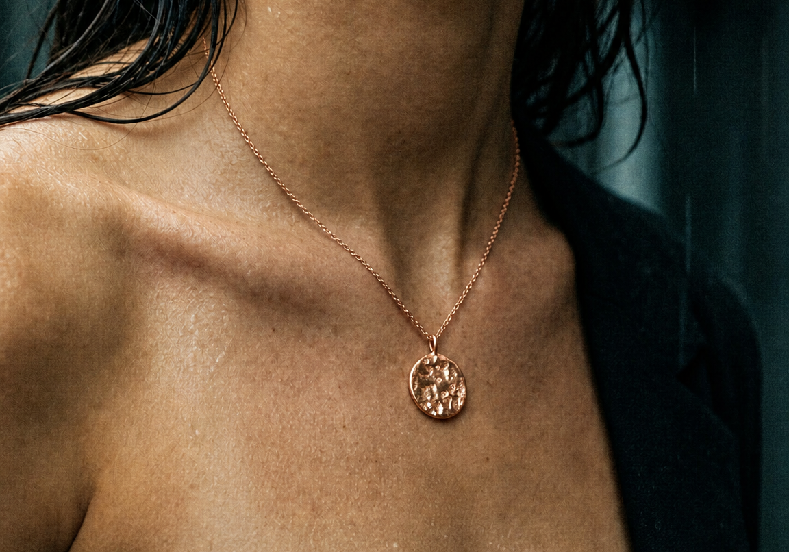 Close-up of a woman wearing a refined rose gold necklace with a stone set pendant.
