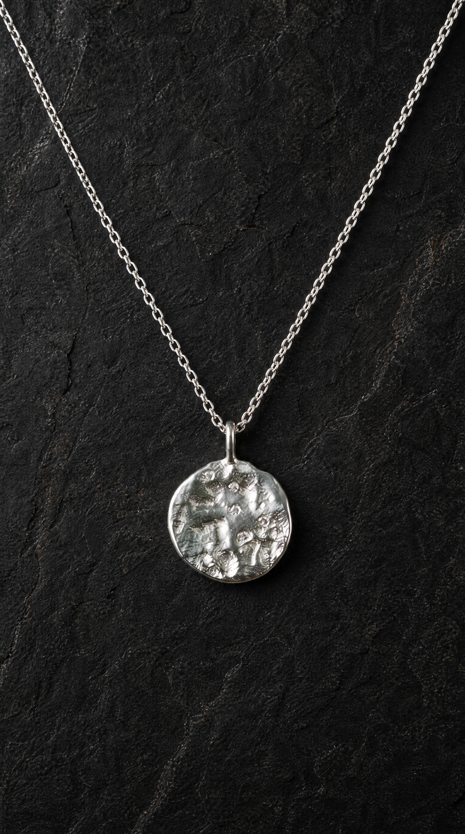 Refined Silver necklace with a textured stone set pendant on a dark background