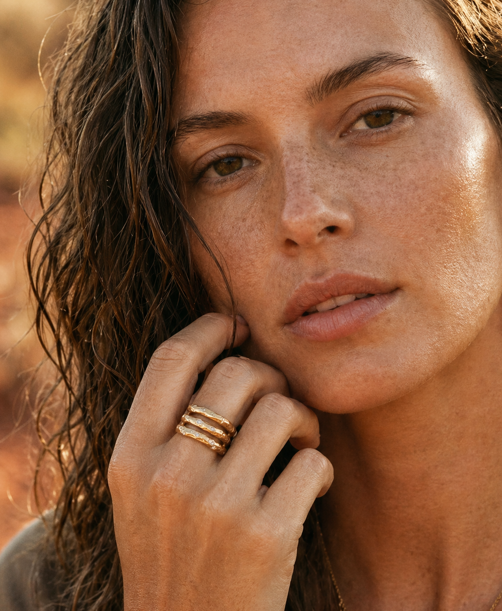 Close-up of a woman with freckles, wearing a raw gold ring, against a blurred natural background.
