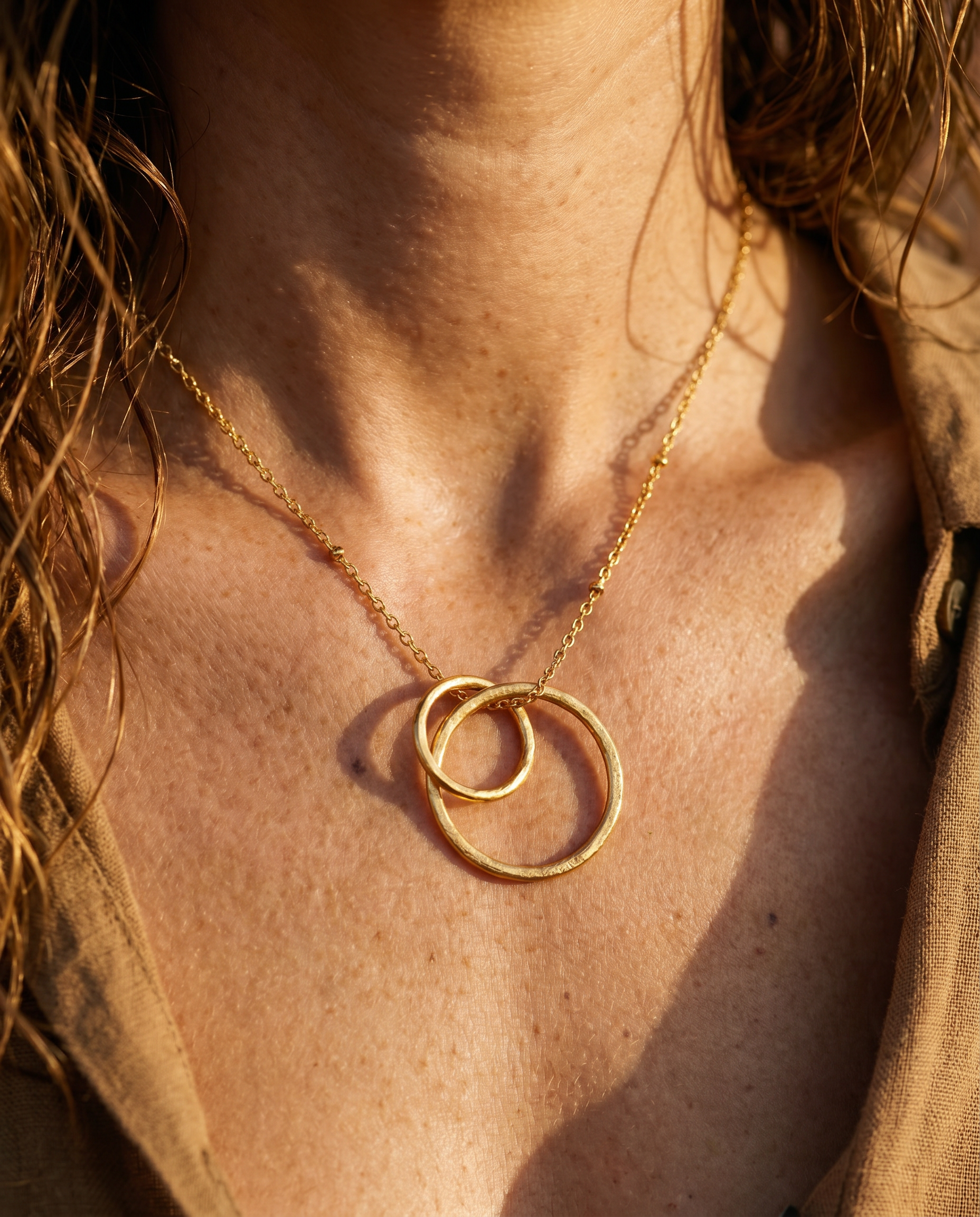 Close-up of a person wearing a delicate gold necklace with interlocking rings.