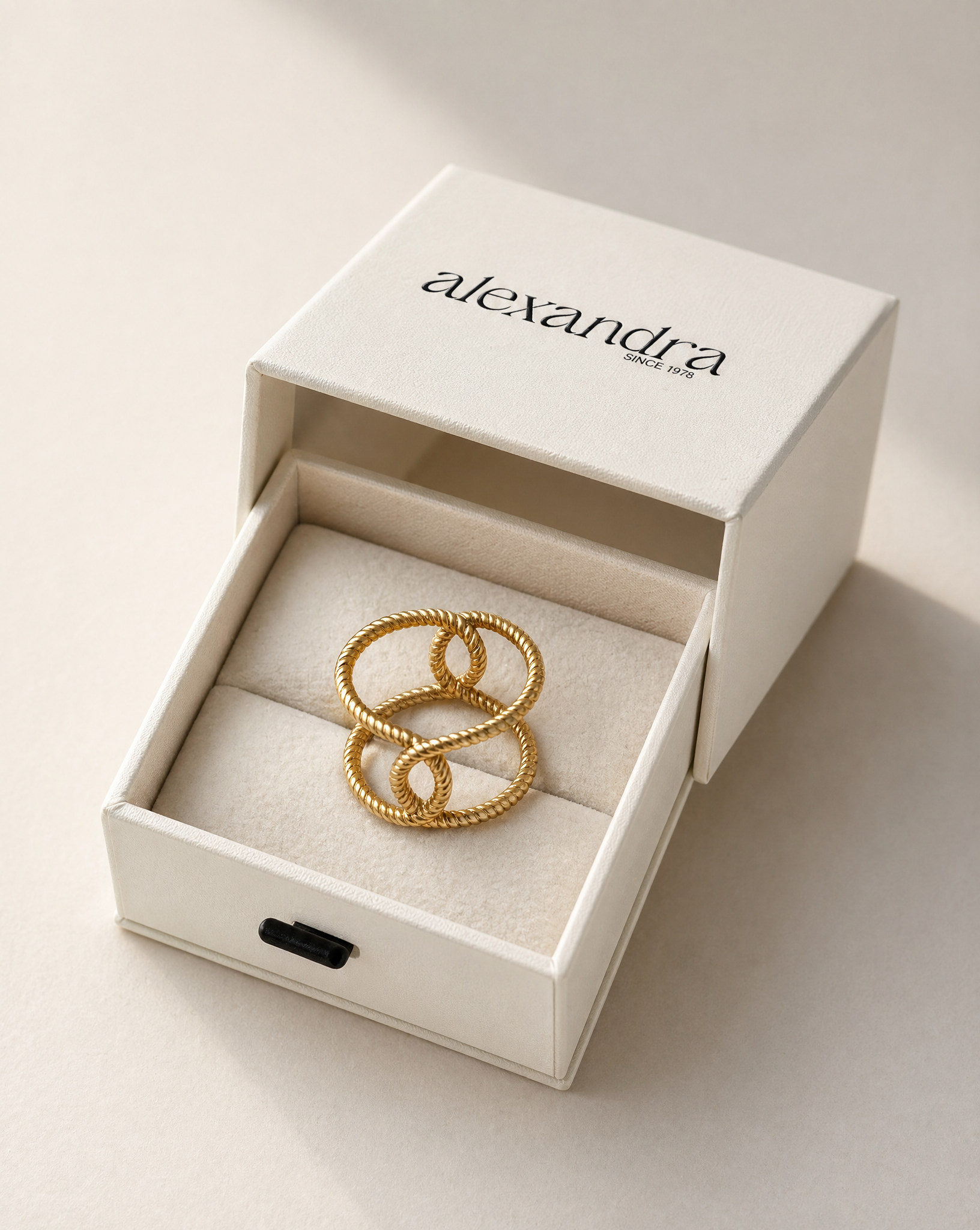 Sculptured gold ring in a 'alexandra' branded box on a light background