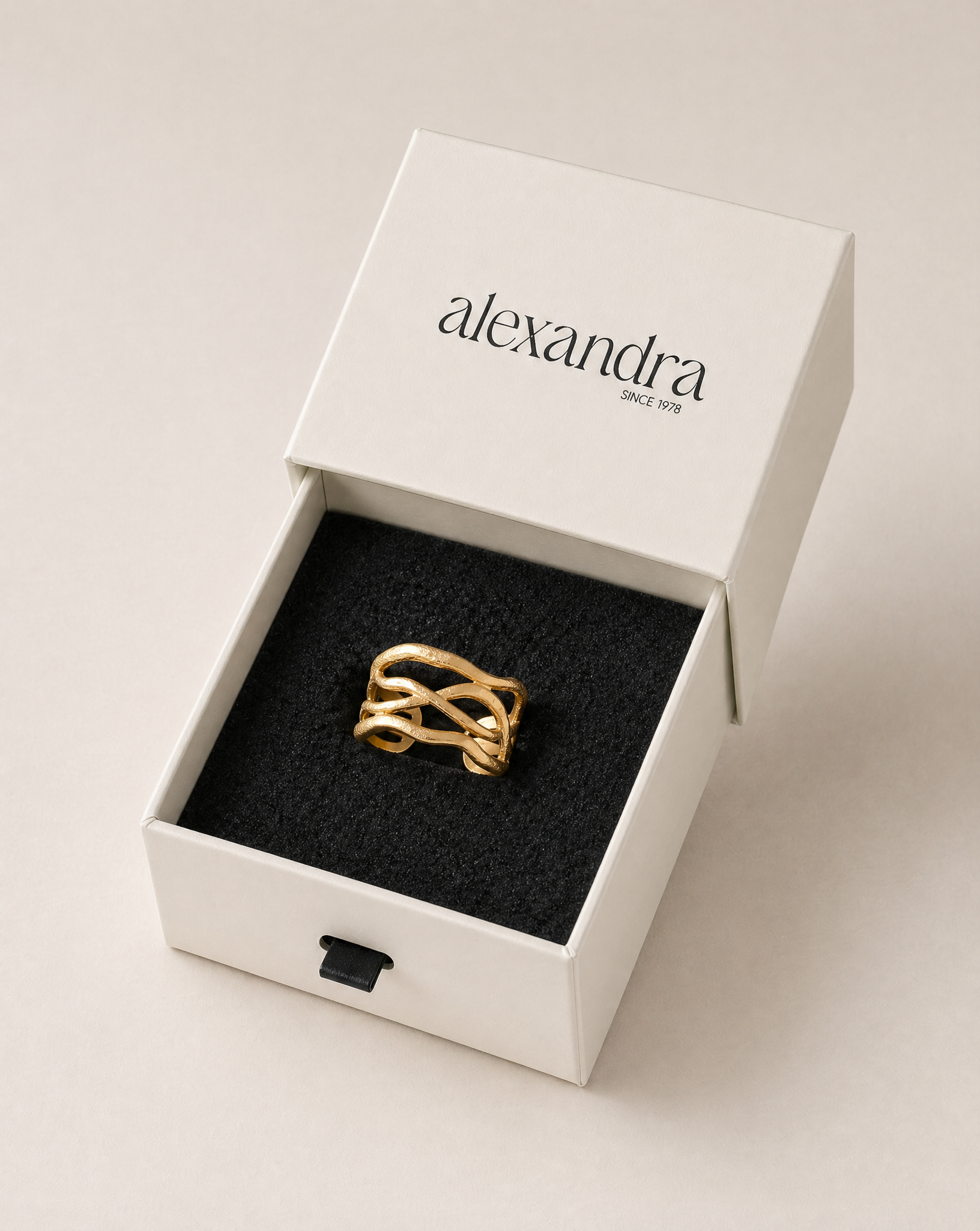 Textured gold ring in a white box with 'alexandra' branding on a light background