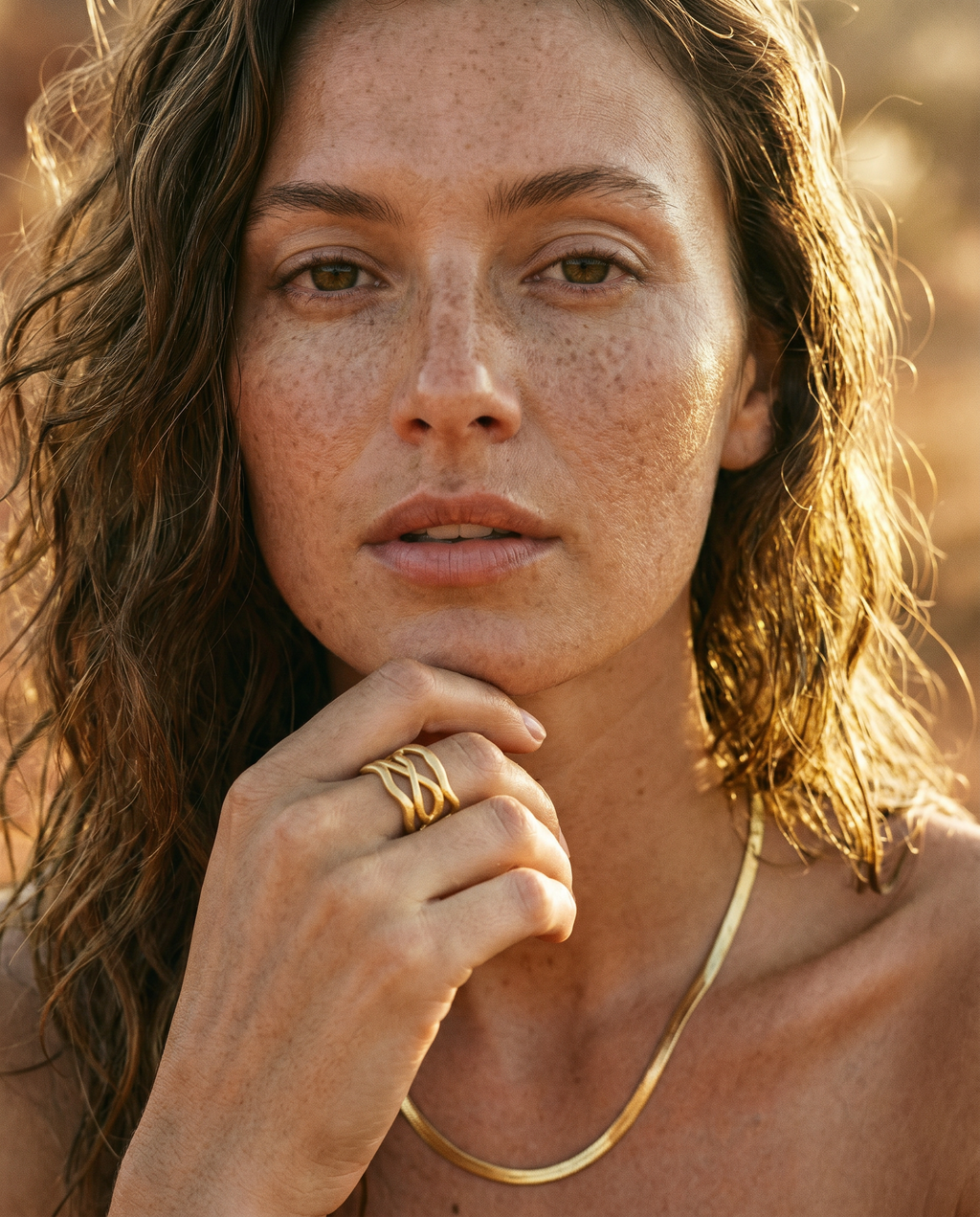 Woman with freckles wearing a refined gold ring against a blurred natural background