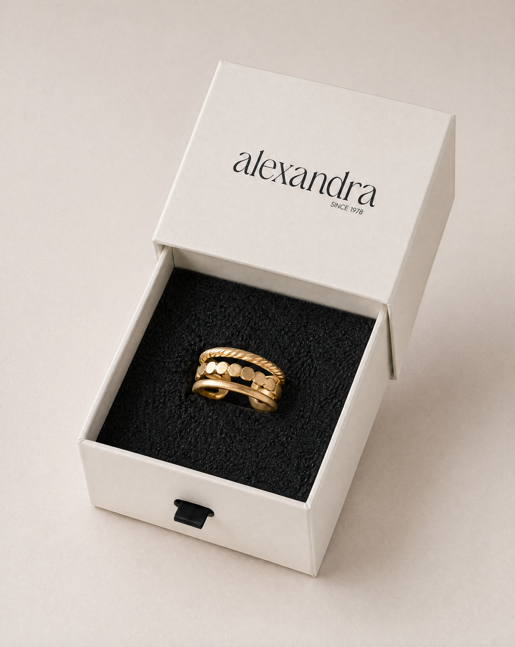 Architectural gold ring in a white box with 'alexandra' branding on a beige background