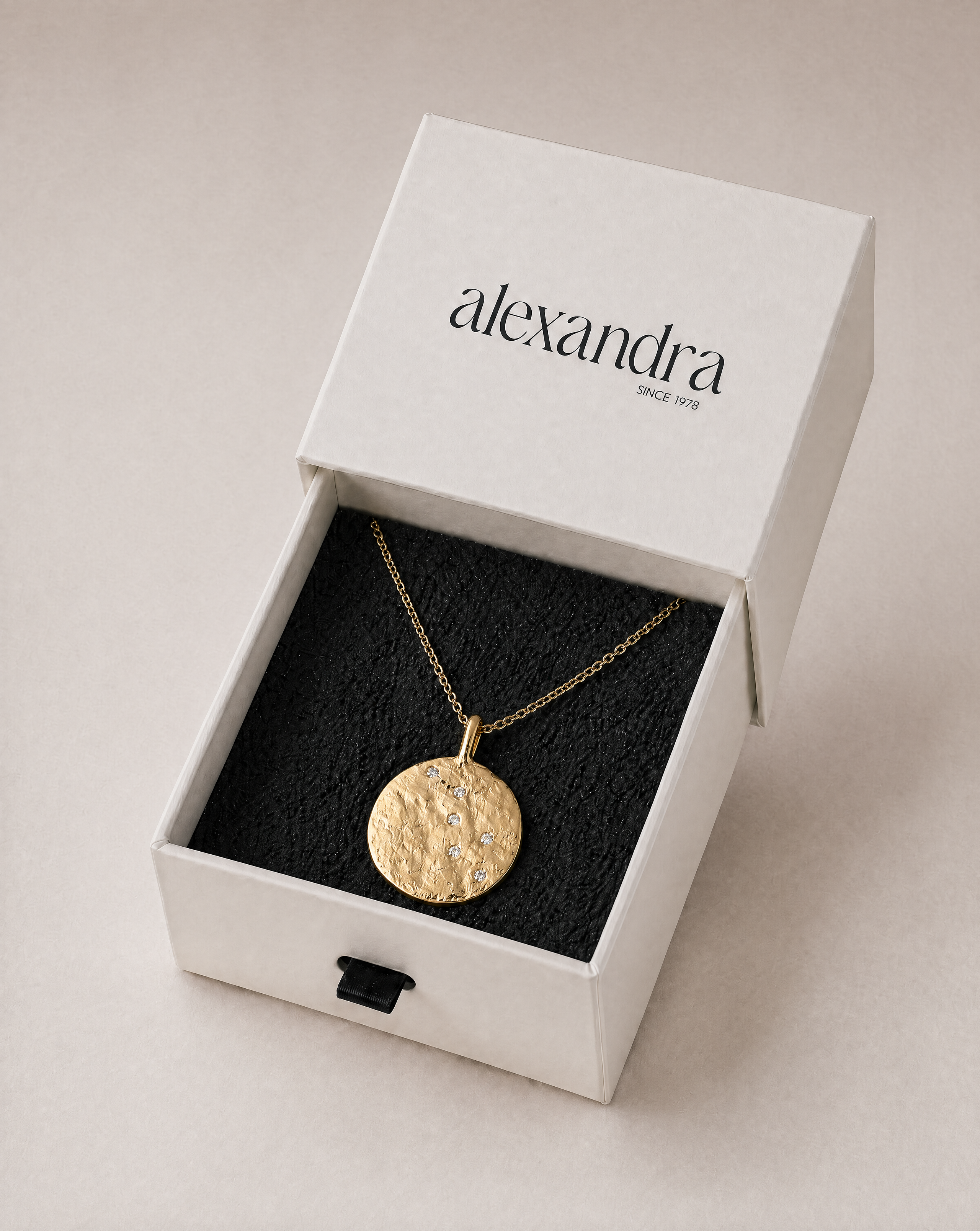 Raw gold necklace in an open 'alexandra' box on a beige background