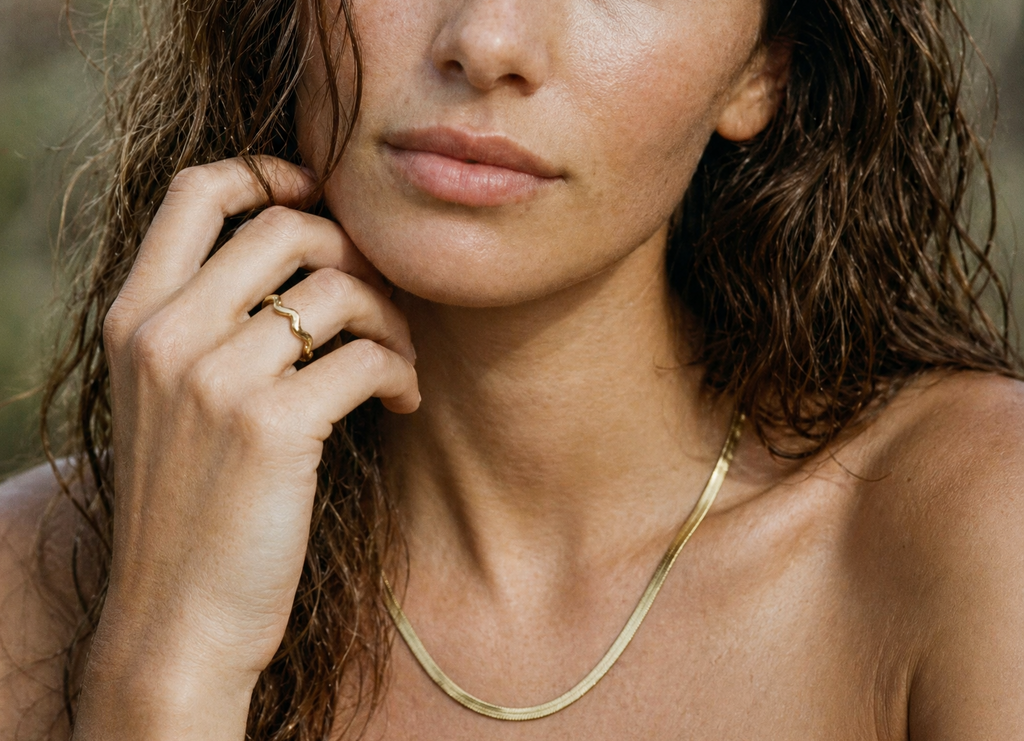 Woman wearing a delicate gold ring and necklace on a blurred natural background