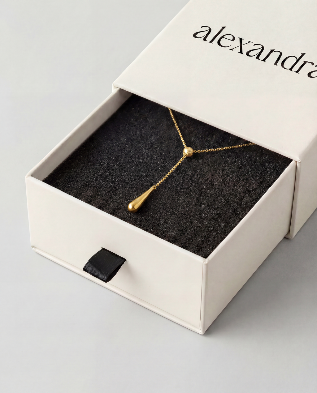 Gold lariat necklace in an open jewellery box with 'alexandra' branding.