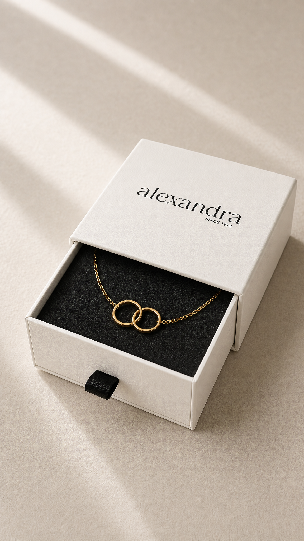 Delicate Gold bracelet with interlocking rings in a white 'alexandra' box on a beige surface