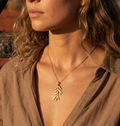 Close-up of woman wearing a sculptural gold necklace with a leaf pendant outdoors.