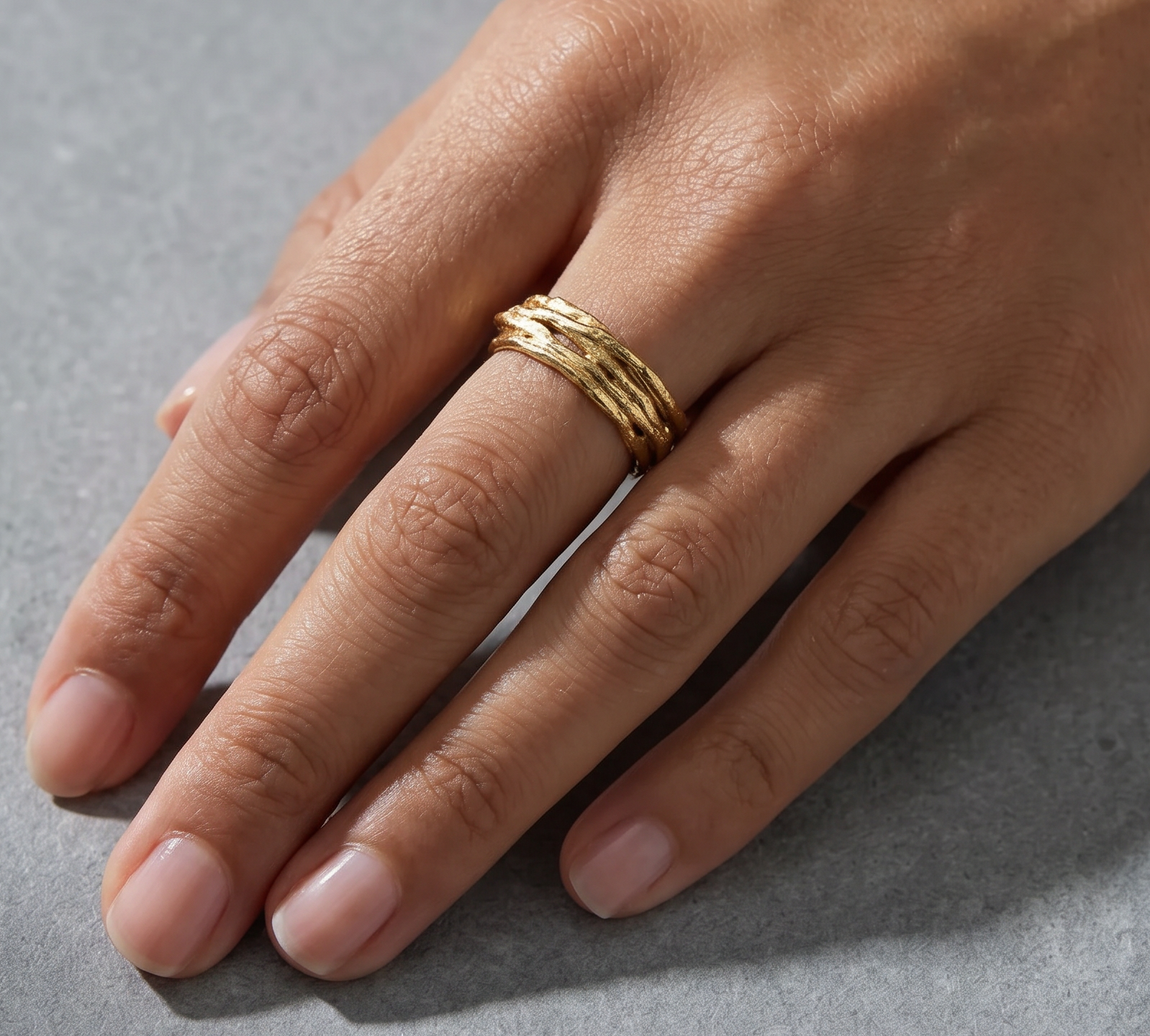 Hand wearing a refined gold ring on a gray background