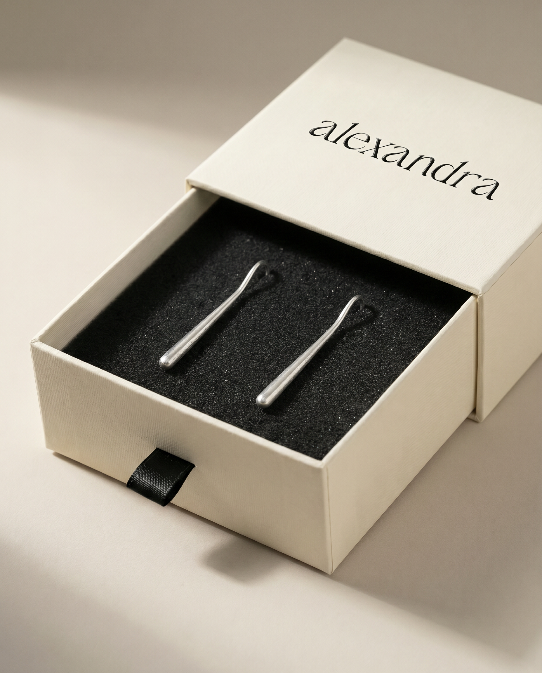 Pair of silver earrings in an open 'alexandra' branded box on a neutral background