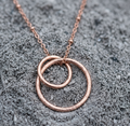 Sculptured Rose gold necklace with interlocking rings on a textured gray surface