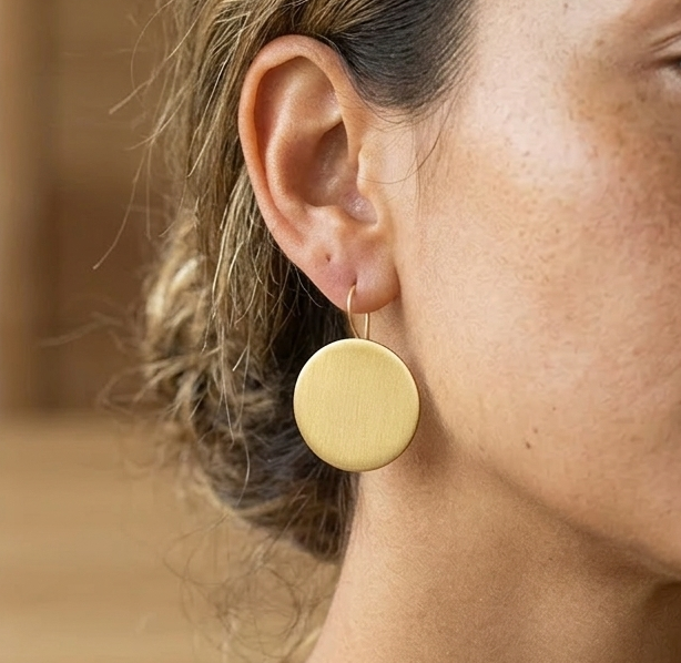 Close-up of a woman wearing a delicate brushed gold round earring with a blurred background