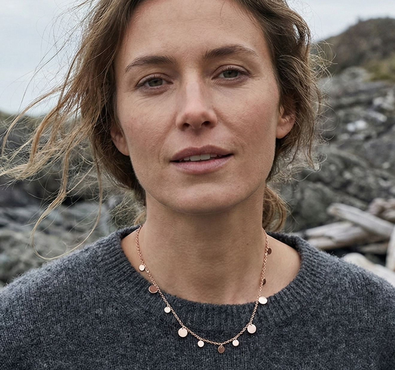 Woman wearing a dark gray sweater with a refined layered rose gold necklace against a rocky background