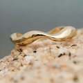 Elevated luxury Gold wavy ring on a textured surface with a blurred background