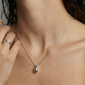 Woman wearing a soft formed silver necklace with a teardrop pendant, hand resting on her shoulder.