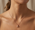 Sculptural Rose gold necklace with a teardrop pendant on a woman's neck against a neutral background