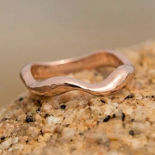 Delicate Rose gold wavy ring on a textured stone surface with a blurred background