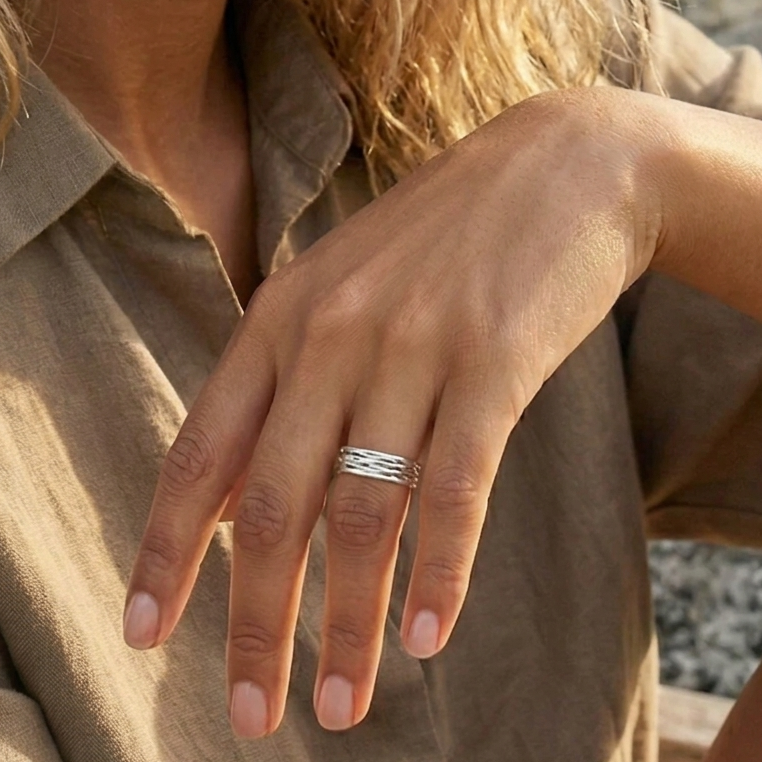 Close-up of a hand wearing a delicate silver ring with a blurred natural background