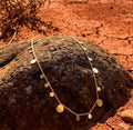 Refined Gold necklace with disc pendants on a textured rock with a red-earth background