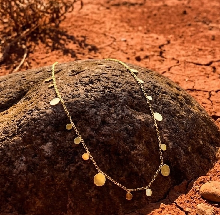 Refined Gold necklace with disc pendants on a textured rock with a red-earth background
