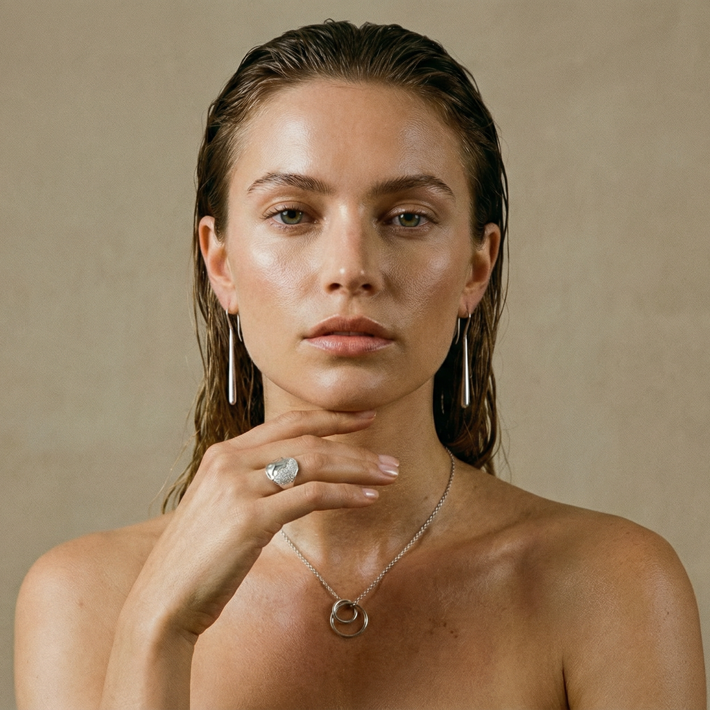 Woman wearing delicate silver earrings and a necklace against a beige background
