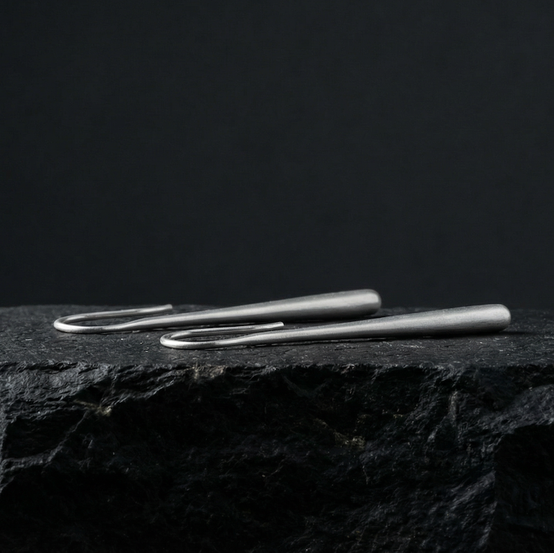 Pair of refined silver drop earrings on a black stone surface with a black background