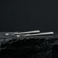 Pair of refined silver drop earrings on a black stone surface with a black background